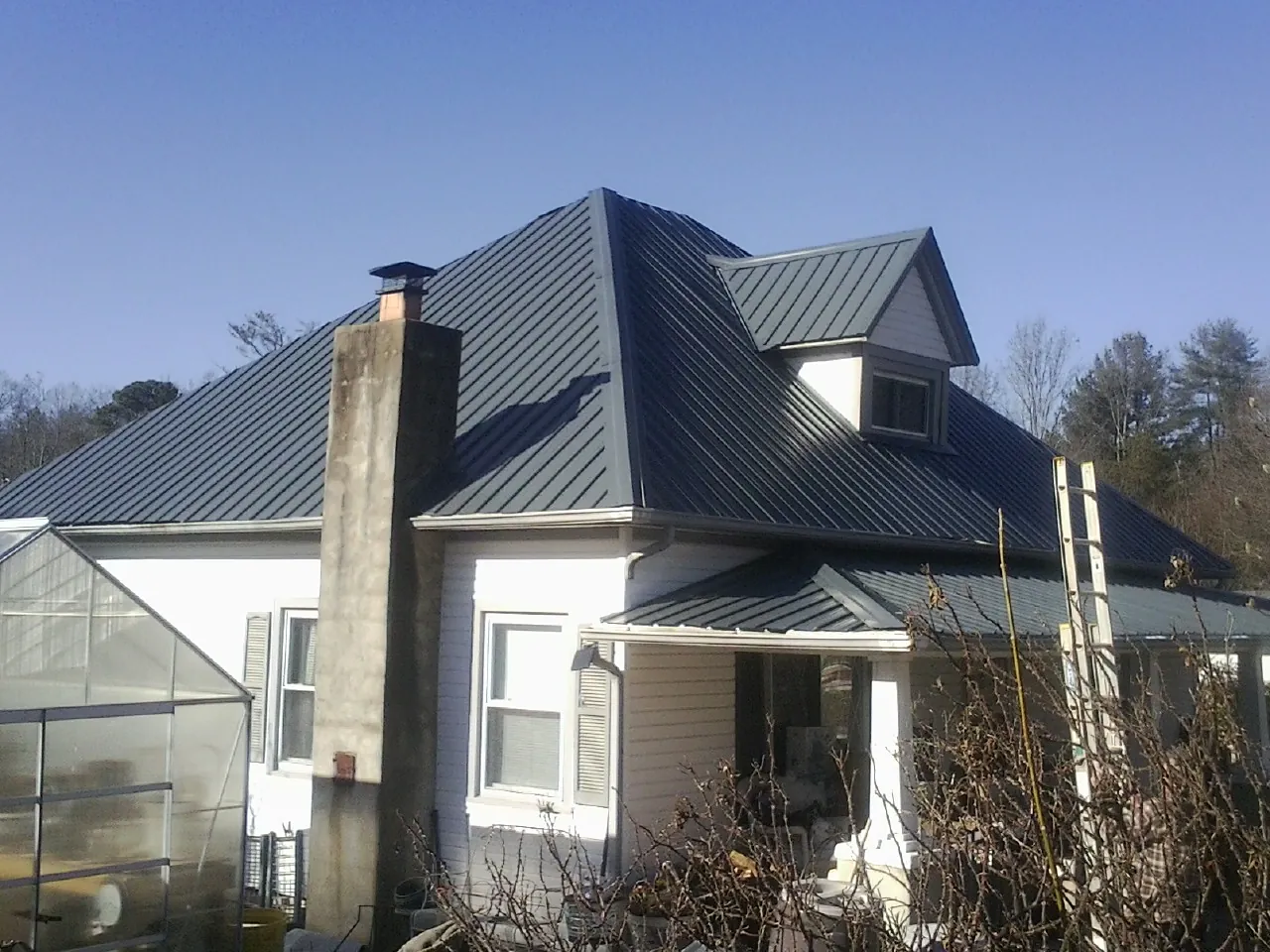 Dark blue standing seam metal roof on a white farmhouse with dormer — Slate & Tile Roof Repair by Roofing Brothers in Baraboo
