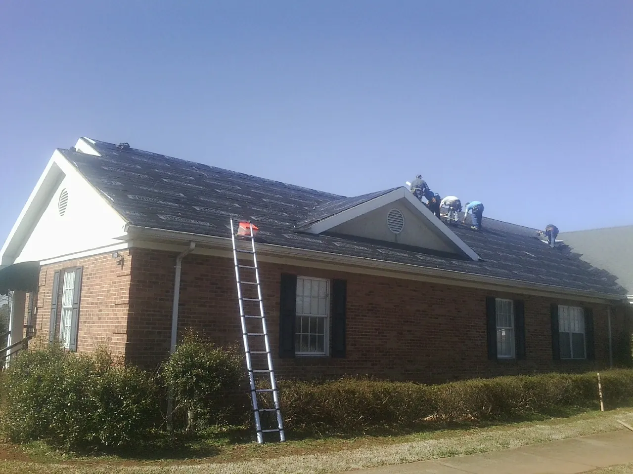Crew tearing shingles off a brick ranch roof with a ladder set — Emergency Roof Repair work by our crew in Baraboo