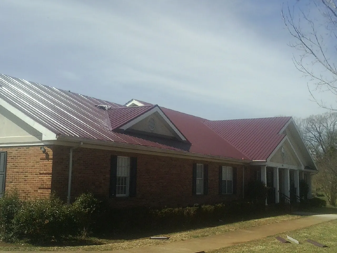 Red metal roof with gabled entries on a long brick building, from a Hail Damage Roof Repair job in Baraboo