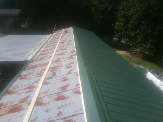 Old rusted panels beside newly installed green metal roofing — Wind Damage Roof Repair by Roofing Brothers in Baraboo