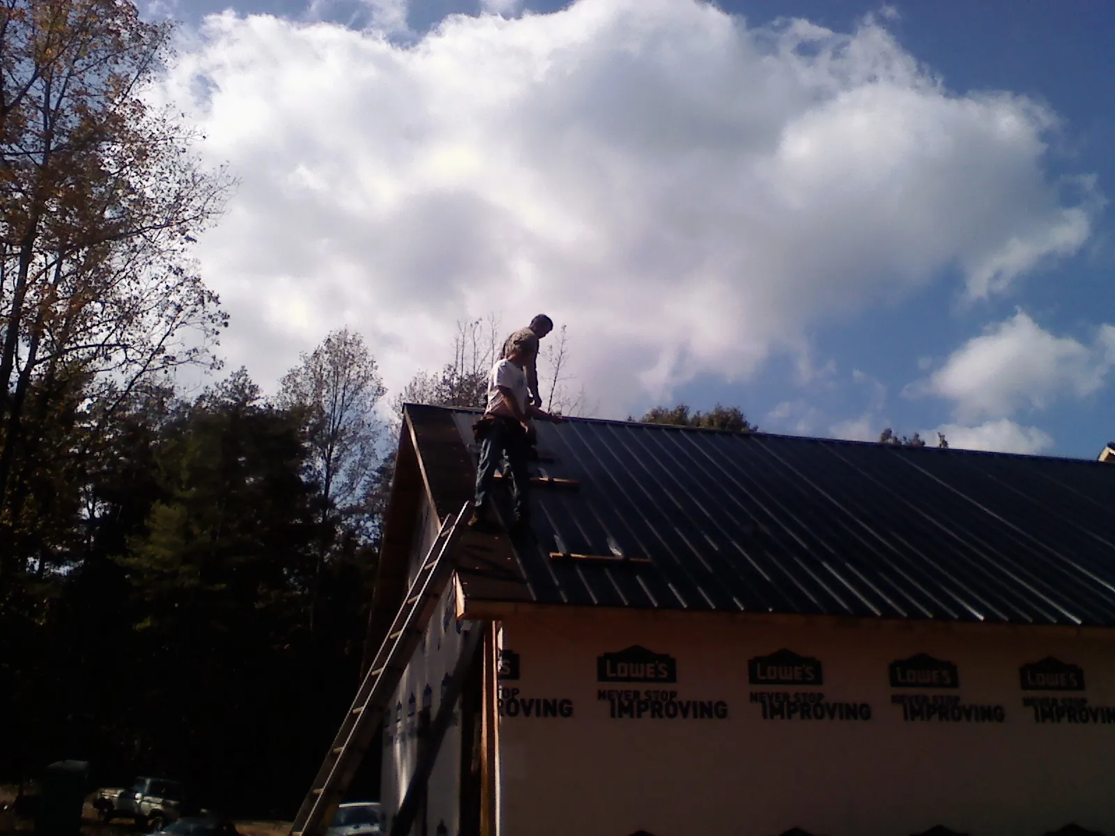 Roofer fastening dark metal panels high against a cloudy sky, from a Roof Inspection job in Baraboo