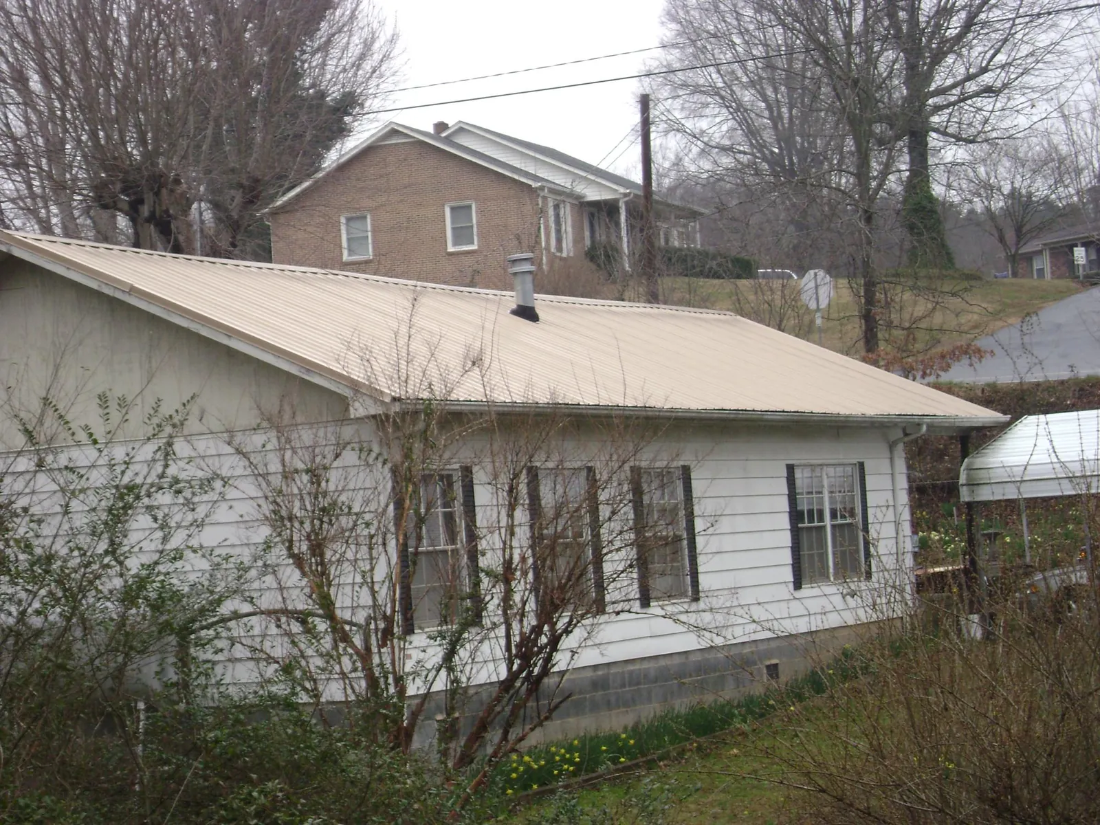 Tan metal roof on a white sided house set into a hillside — Commercial Roofing by Roofing Brothers in Baraboo