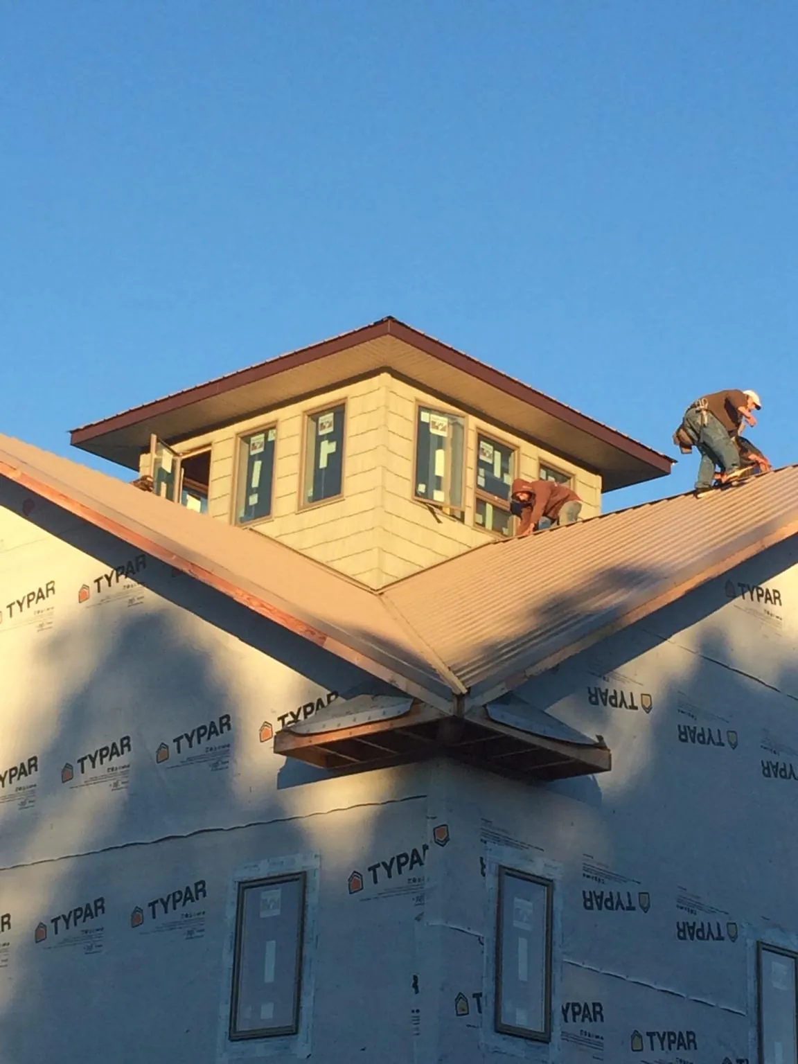 Roofers working around a rooftop cupola on a new metal roof at sunset — Roof Waterproofing in Baraboo by Roofing Brothers